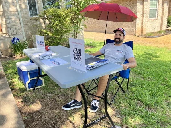 Zach at an outdoor table with Zach’s Transport & Assembly business materials and signage