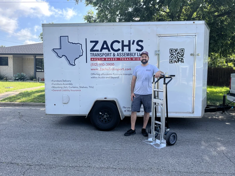 Zach standing beside his branded Zach’s Transport & Assembly trailer with a hand truck